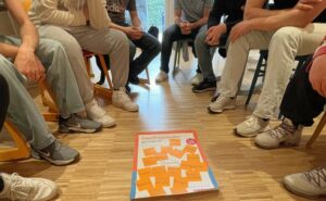 Stuhlkreis mit Jugendlichen und Plakat Aktion Mensch auf dem Boden
