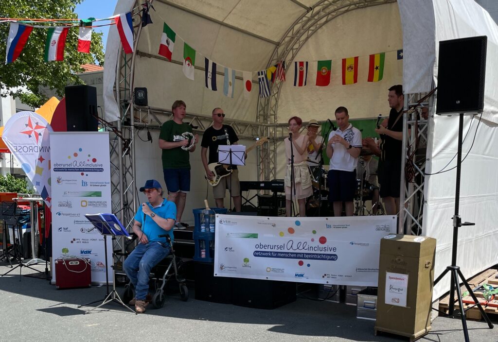 Eine inklusive Band spielt auf einer Bühne mit internationalen Flaggen im Hintergrund bei einer Veranstaltung von oberursel all inclusive