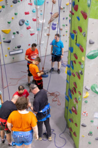 Mehrere Personen mit Klettergurten bereiten sich an einer Kletterwand mit bunten Griffen vor