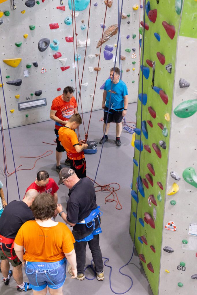 Mehrere Personen mit Klettergurten bereiten sich an einer Kletterwand mit bunten Griffen vor